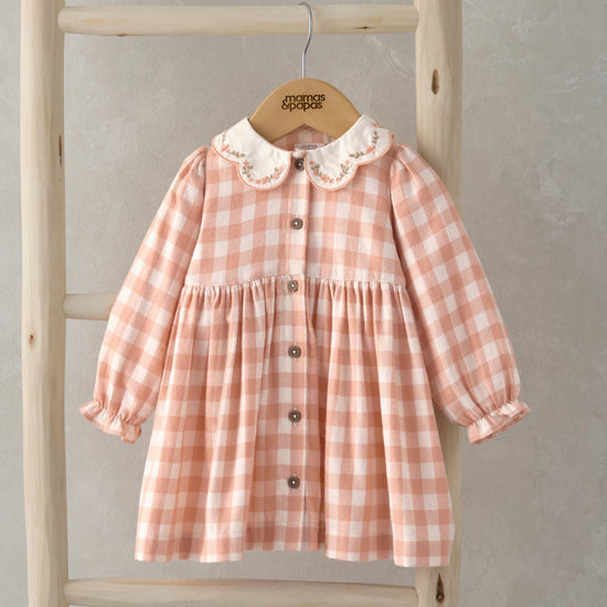 A pink checkerboard dress with collar detail is hanging on a wooden ladder.