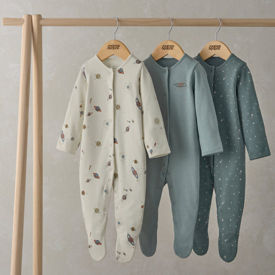 Three coordinating baby sleepsuits are hanging from a wooden rail.