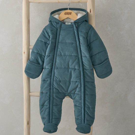 A blue quilted pramsuit is hanging on a wooden ladder.