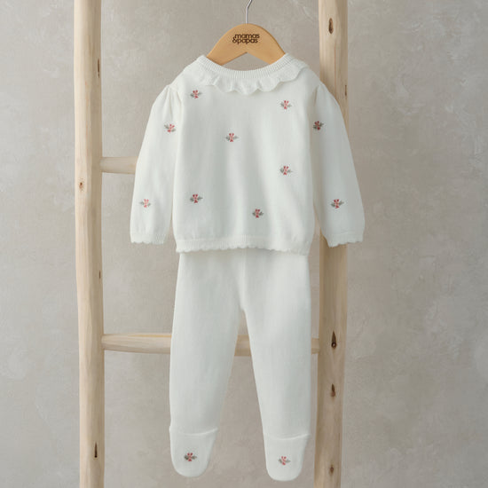 A white knitted jumper and leggings with pink pattern are hanging on a wooden ladder.