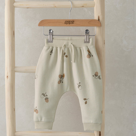 A pair of baby joggers with an acorn print are hanging on a wooden ladder.