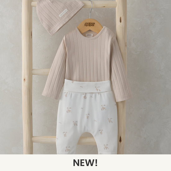 A beige bodysuit, leggings and hat set are hanging from a wooden ladder. 